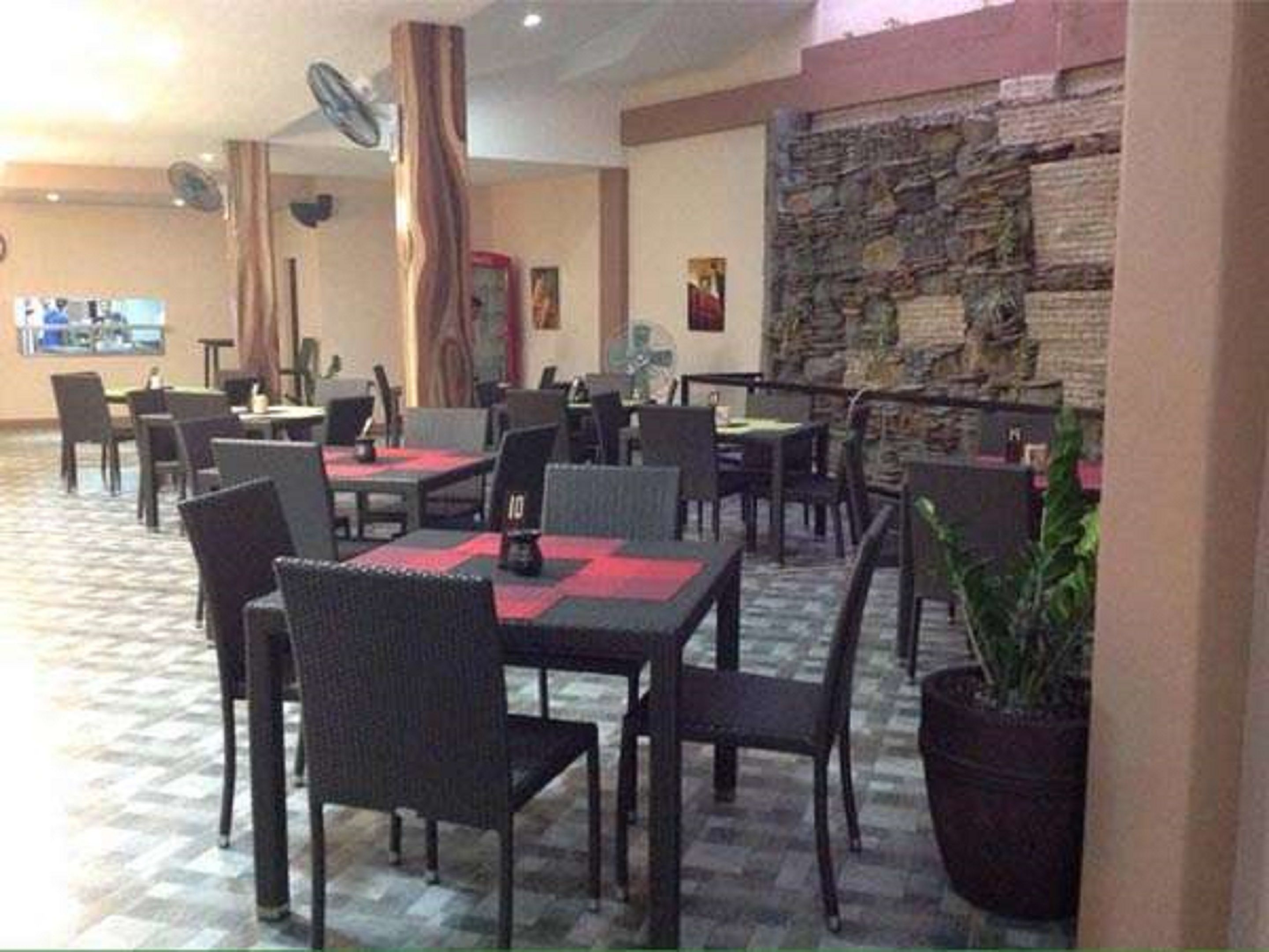 A restaurant with multiple tables and chairs, a stone wall, and a fan on the ceiling.
