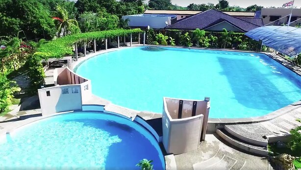 A large, clear swimming pool with a curved design, surrounded by lush greenery and shaded areas. - Buddha Resort by Cocotel (Bugallon)