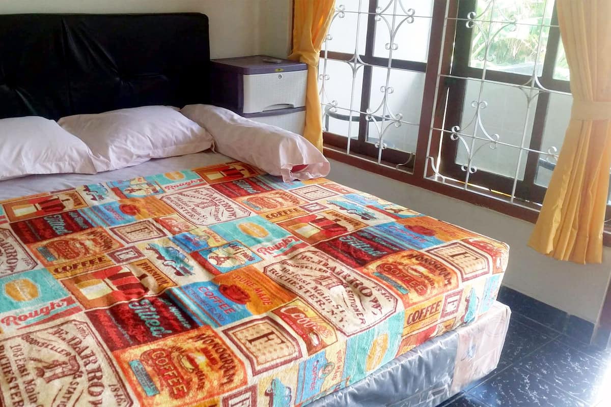 A bed with a colorful quilt, a black headboard, a nightstand with a lamp, and a window with metal bars and curtains.
