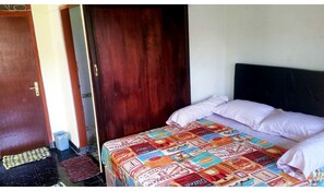 A bedroom with a bed covered in a colorful blanket, a wooden door, and a small rug on the floor. - Morotai Camp Hostel -Adult Only (Denpasar)