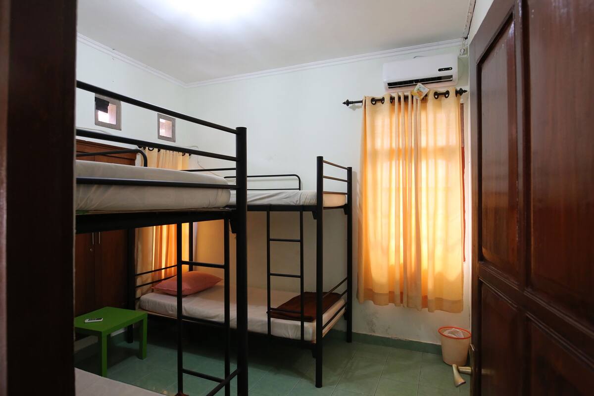 A bunk bed room with a small table, a curtain, and an air conditioning unit.
