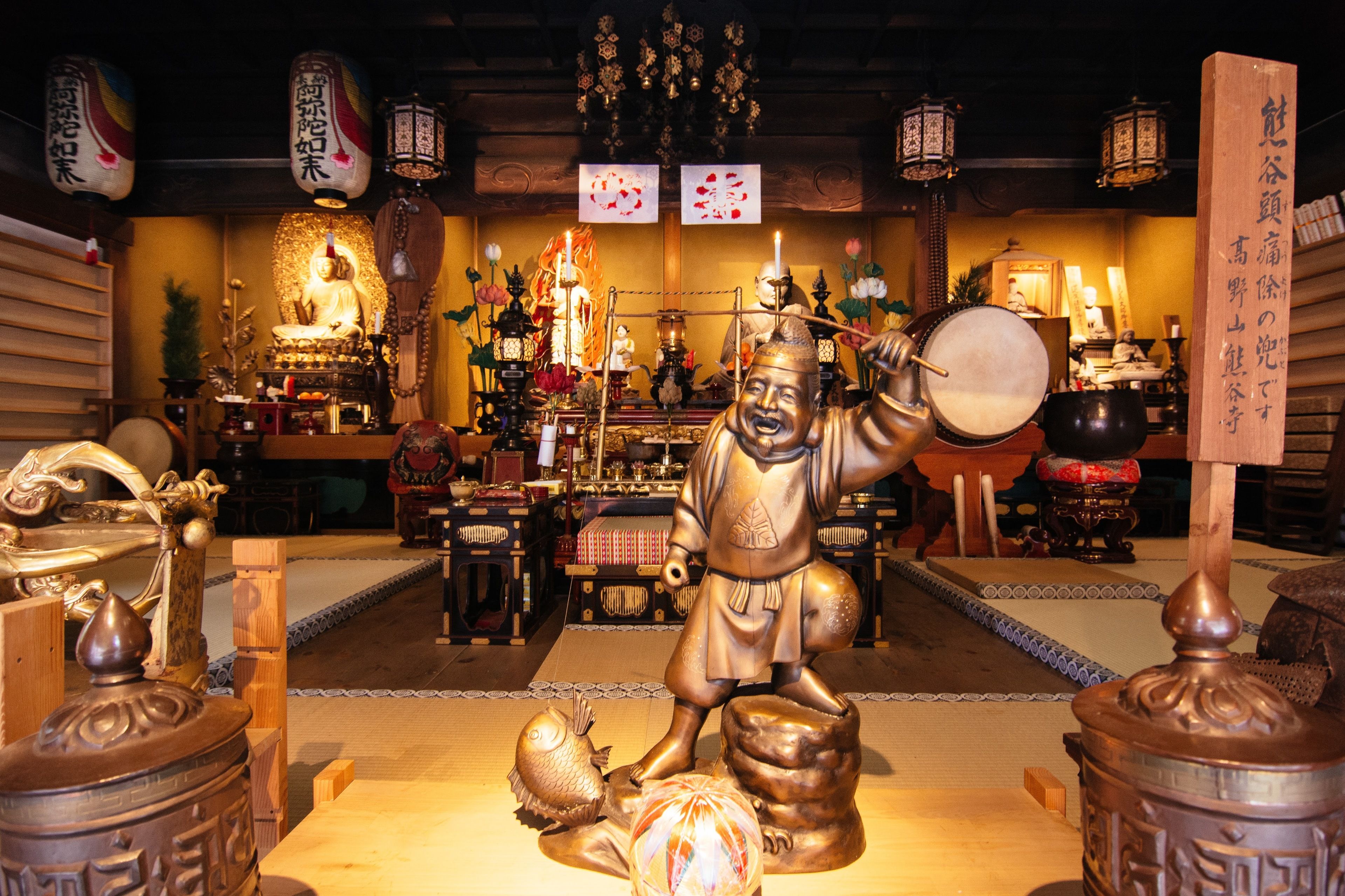 A traditional Japanese shrine with a statue of a figure holding a drum, surrounded by various religious artifacts and offerings.