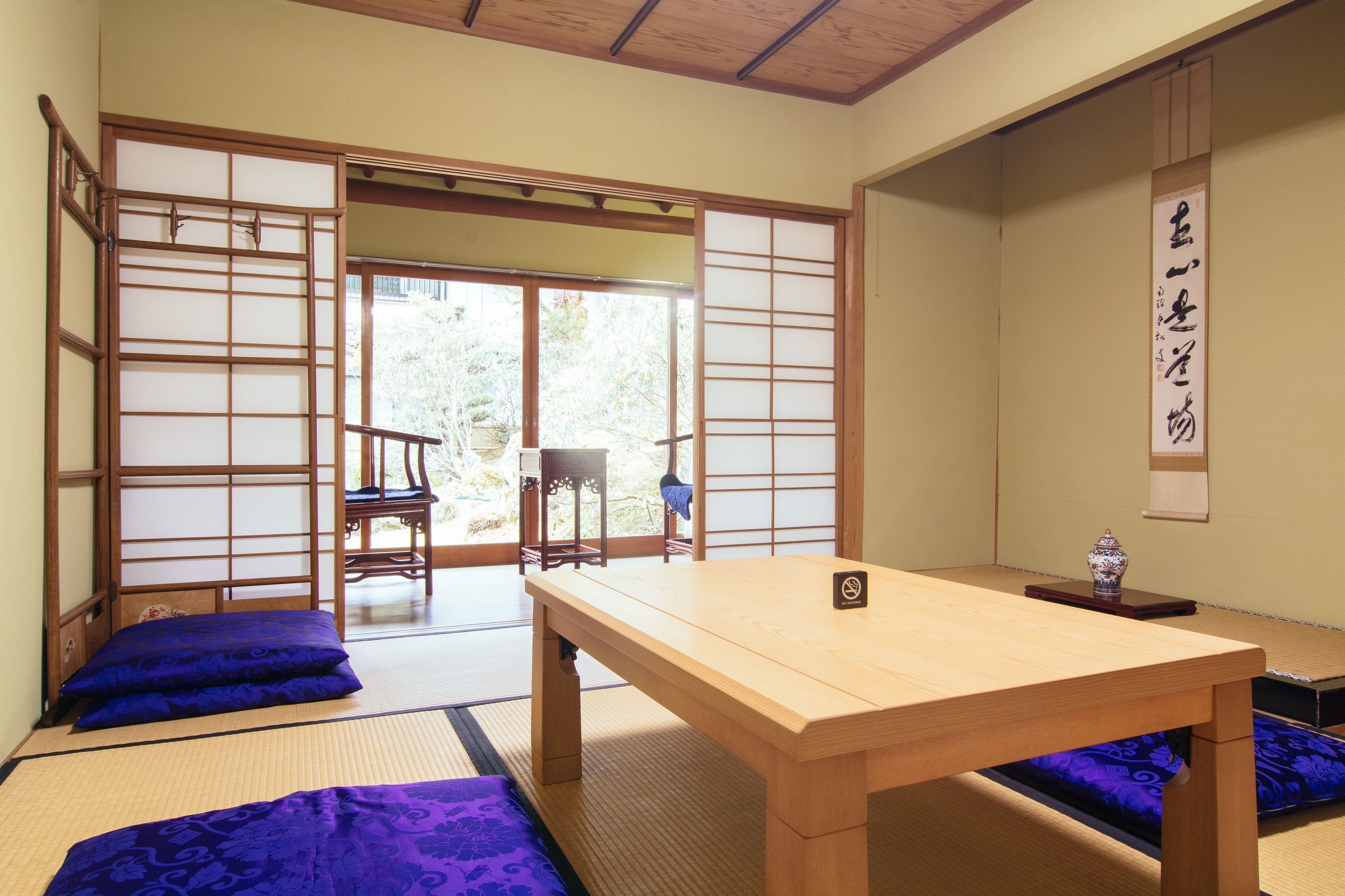 A traditional Japanese room with tatami flooring, a low wooden table, and a sliding door leading to an outdoor area.