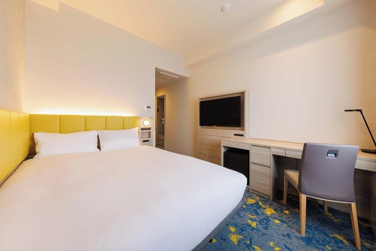 Ein Hotelzimmer mit einem großen Bett, einem Schreibtisch, einem Stuhl, einem Flachbildfernseher und einem kleinen Fernseher auf einem Schrank.