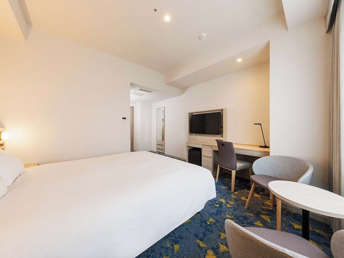A hotel room with a large bed, a desk with a chair, a television, and a small table.