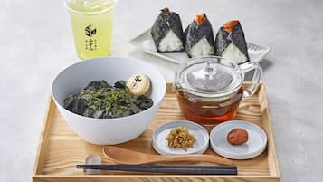 A tray with a bowl of seaweed salad, a cup of tea, and three sushi pieces on a wooden tray.