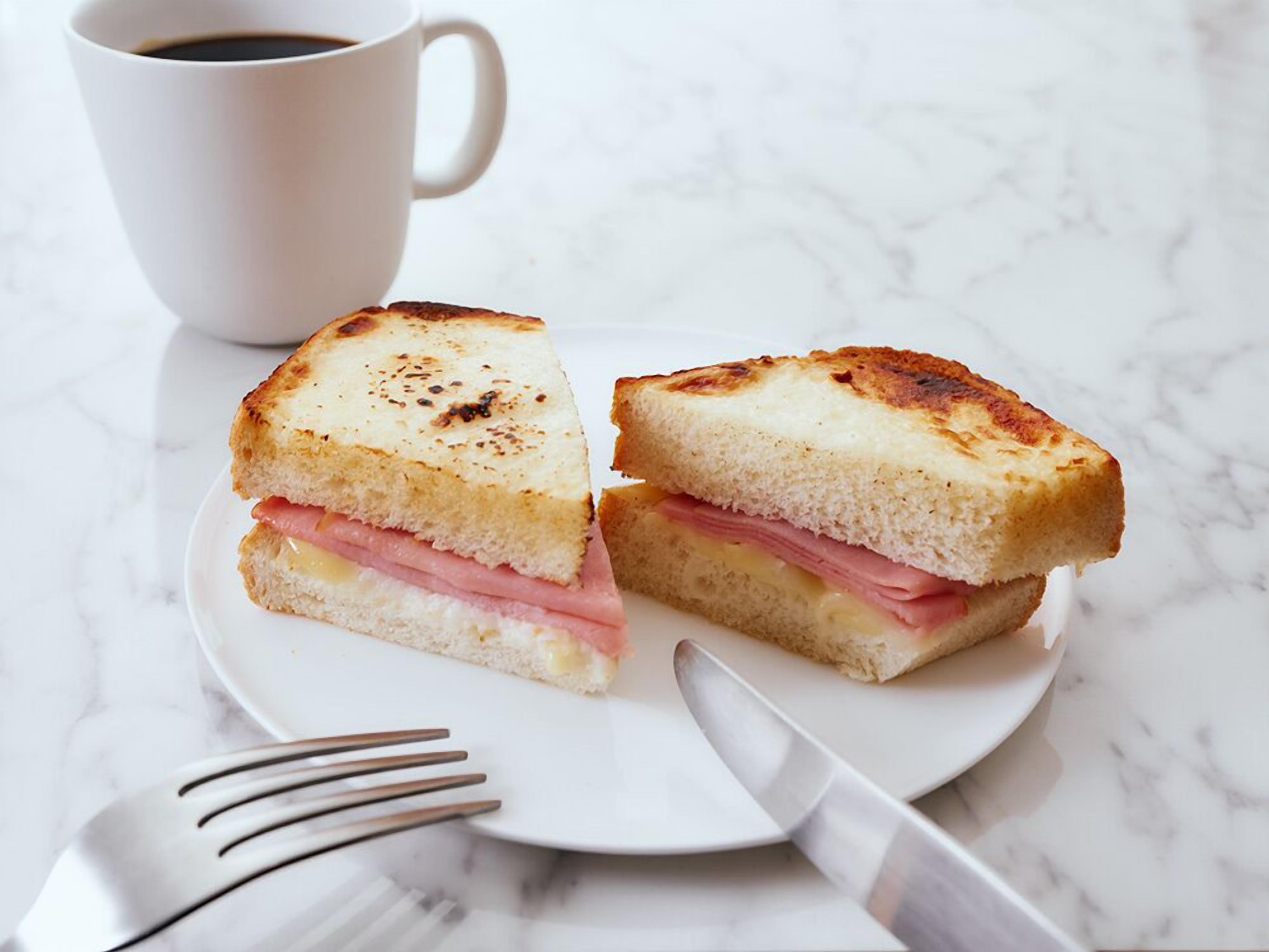 A grilled sandwich cut in half on a white plate, with a fork and knife beside it.