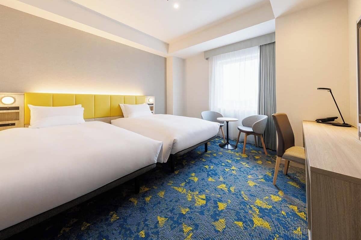 Ein Hotelzimmer mit zwei Betten, einem Schreibtisch, einem Stuhl und einem kleinen Tisch.