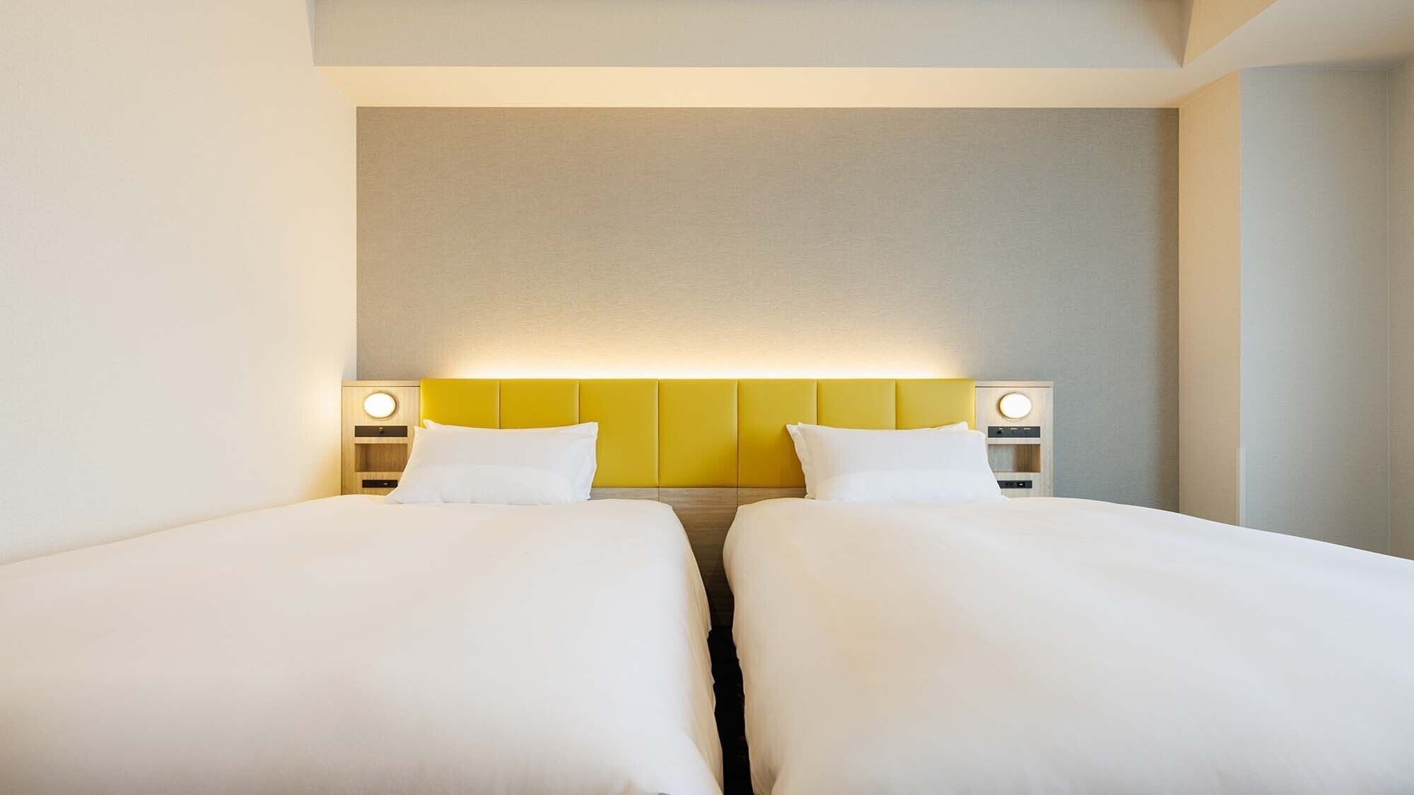 Een hotelkamer met twee bedden, een hoofdbord in neutrale tinten en bedlampjes.