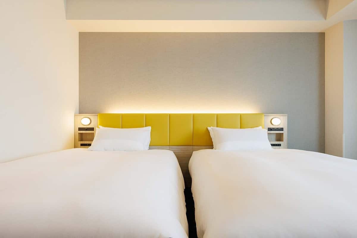 Ein Hotelzimmer mit zwei Betten, einem schlichten Kopfteil und Nachttischlampen.