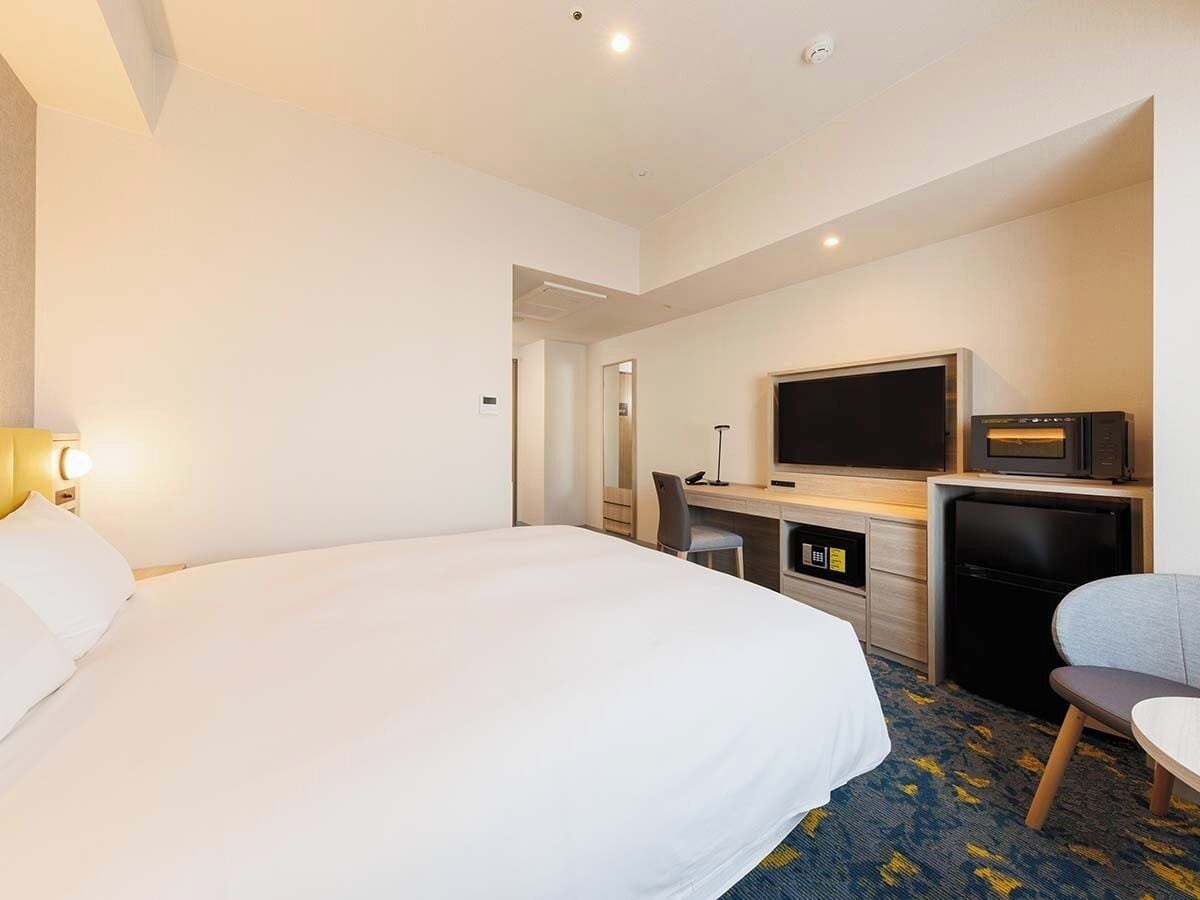 Una habitación de hotel con una cama grande, un escritorio con computadora, televisión y microondas.