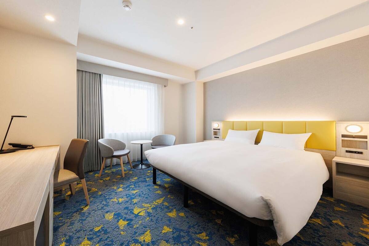 Una habitación de hotel con cama, escritorio, silla y una mesita.