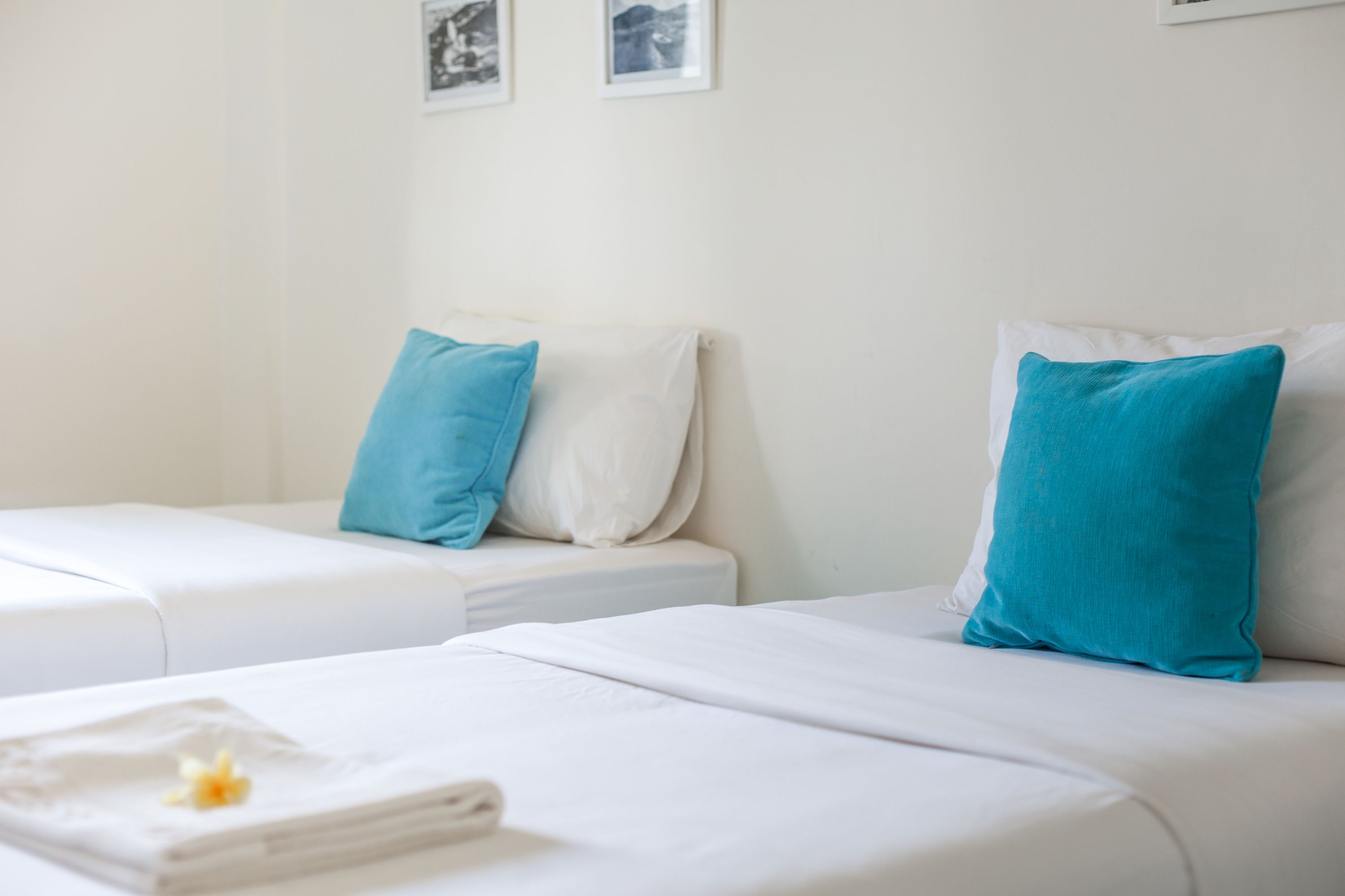 Ein Hotelzimmer mit zwei Betten, jeweils mit weißer Bettwäsche und einem Kopfkissen. Ein kleiner Tisch mit einem Handtuch und einer Blume steht daneben.