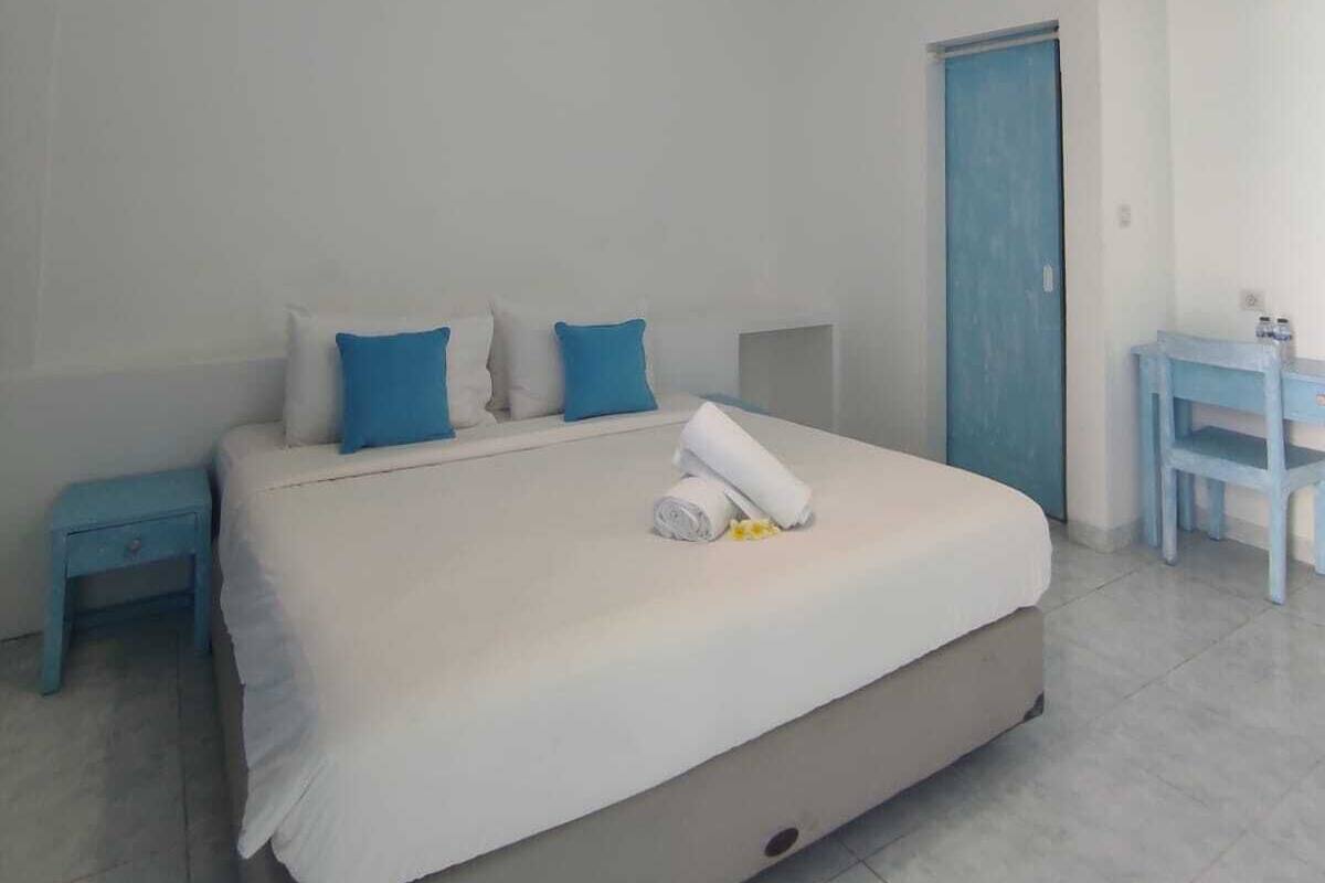 A bedroom with a bed, pillows, a bedside table, a desk, and a hanging light fixture.