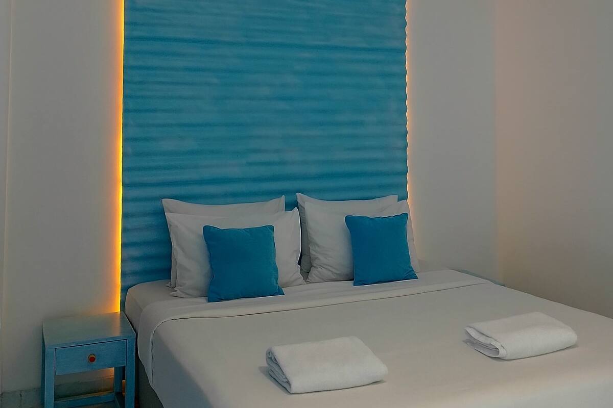 A modern bedroom with a blue accent wall, a white bed, and a hanging light fixture.