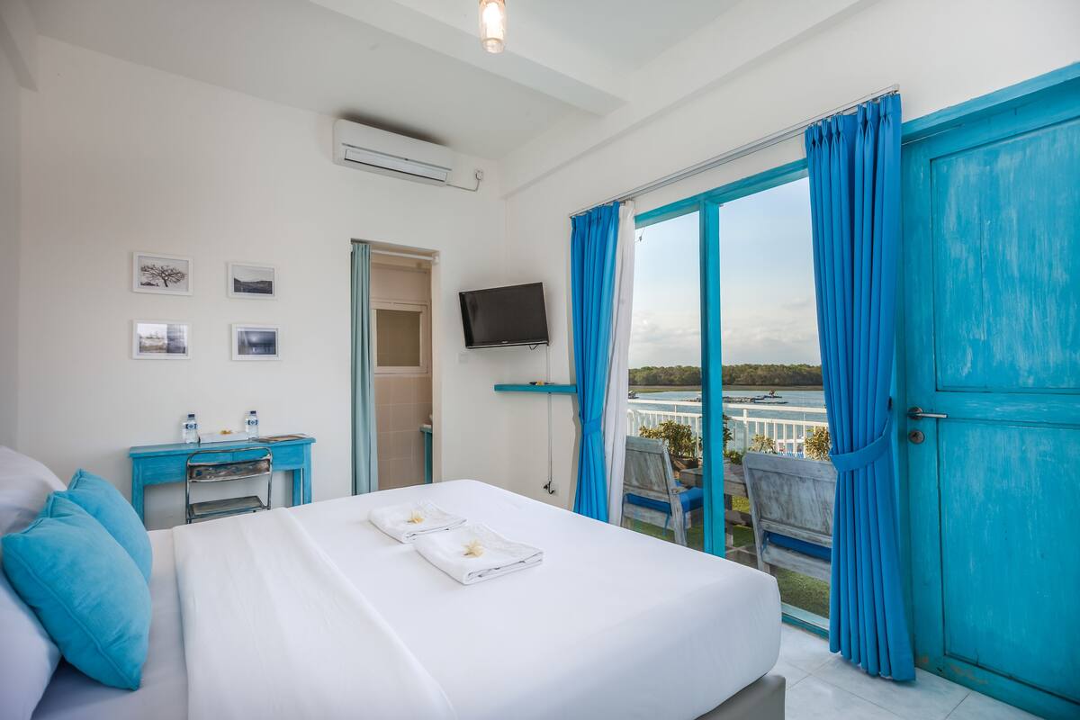 A hotel room with a bed, a desk, a TV, and a balcony with blue curtains.