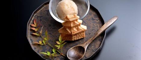 A dessert with a small house-shaped pastry and a scoop of ice cream on a dark plate with a spoon.
