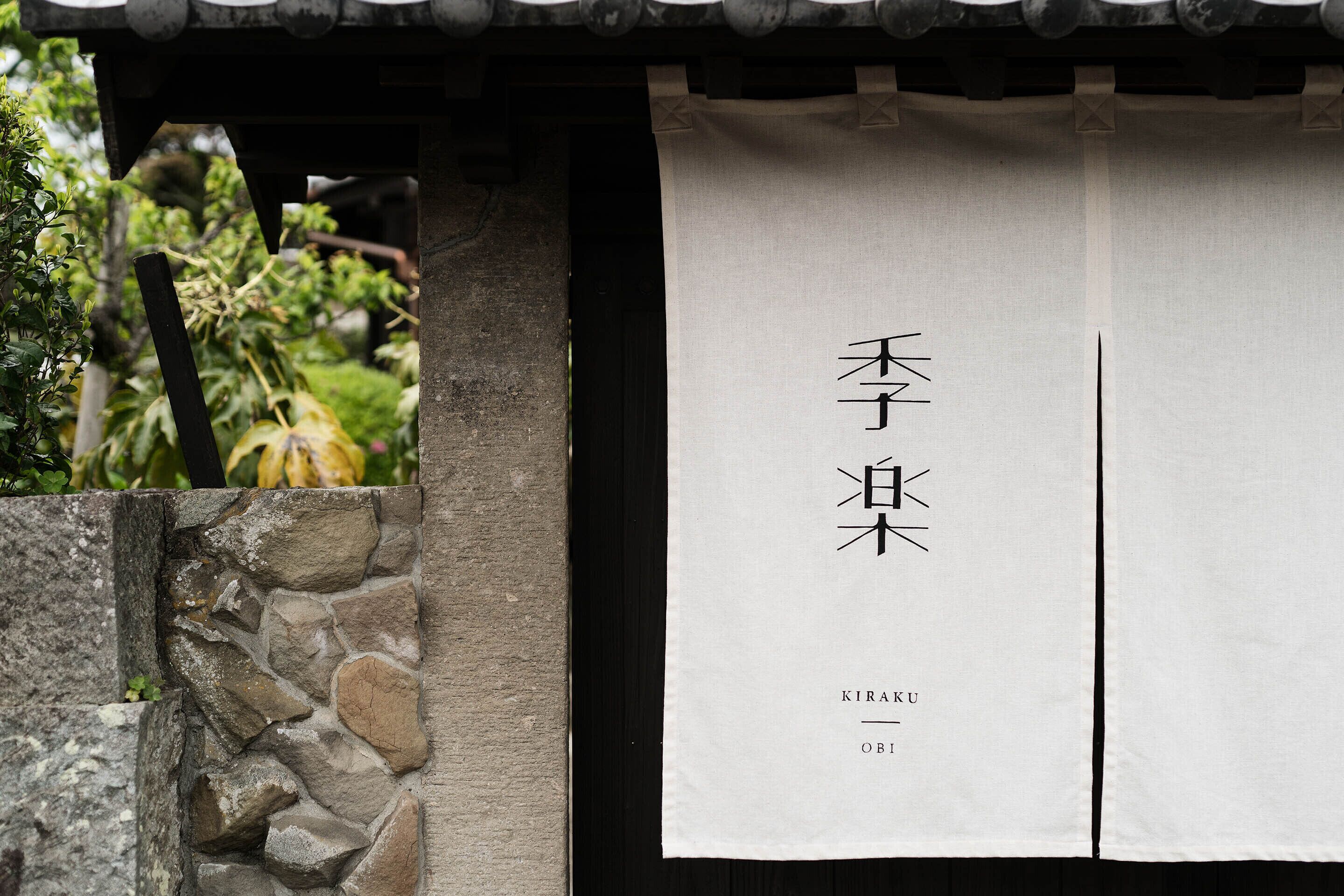 A traditional Japanese building with a stone wall and a hanging white banner with Japanese characters.