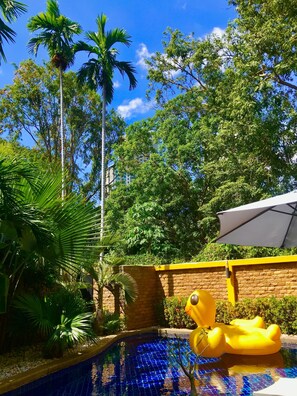 A pool area with a yellow inflatable float, surrounded by palm trees and a brick wall. - 4poolvillas (Pattaya)