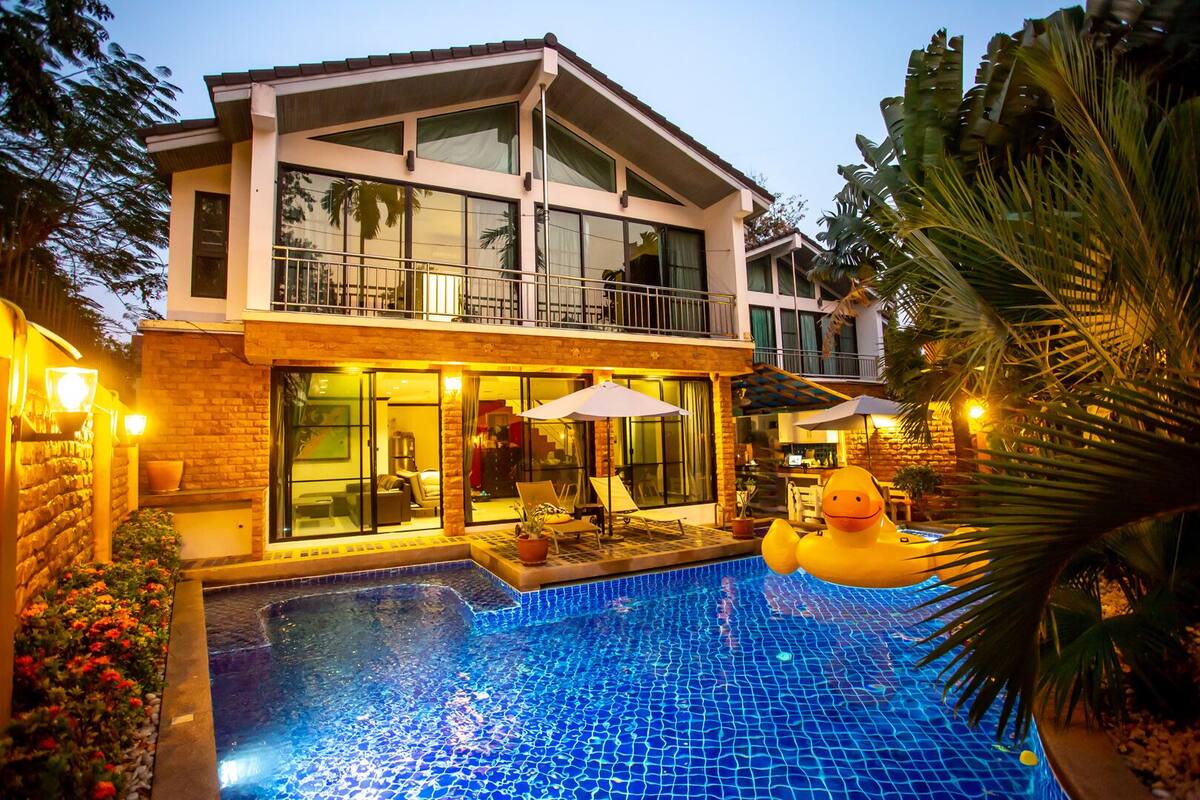 A two-story house with a swimming pool, outdoor furniture, and a large inflatable duck.