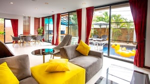 A modern hotel room with a pool view, a dining area, and a living space with a sofa and chairs. - 4poolvillas (Pattaya)
