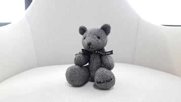 A grey knitted teddy bear with a black ribbon on a white chair.