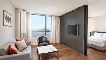 Una habitación de hotel moderna con sofá, sillón, televisión de pantalla plana, cama y ventana grande.