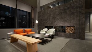 Una sala de estar moderna con una mesa de centro de madera, dos sillas blancas, un sofá naranja y una chimenea con una pared de piedra.