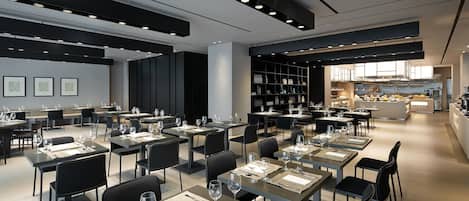 A modern restaurant with multiple dining tables and chairs, a kitchen area in the background, and a clean, minimalist interior design.