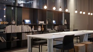 Una sala de conferencias moderna con una mesa larga, sillas negras y una estantería llena de libros y objetos decorativos.