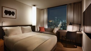 Habitación de hotel con una cama grande, un escritorio y vista a una ciudad iluminada de noche.