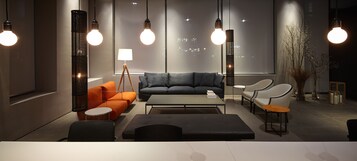 Una sala de estar moderna con un sofá gris, un sillón naranja y una mesa de centro. Se observan lámparas colgantes y una lámpara de pie.