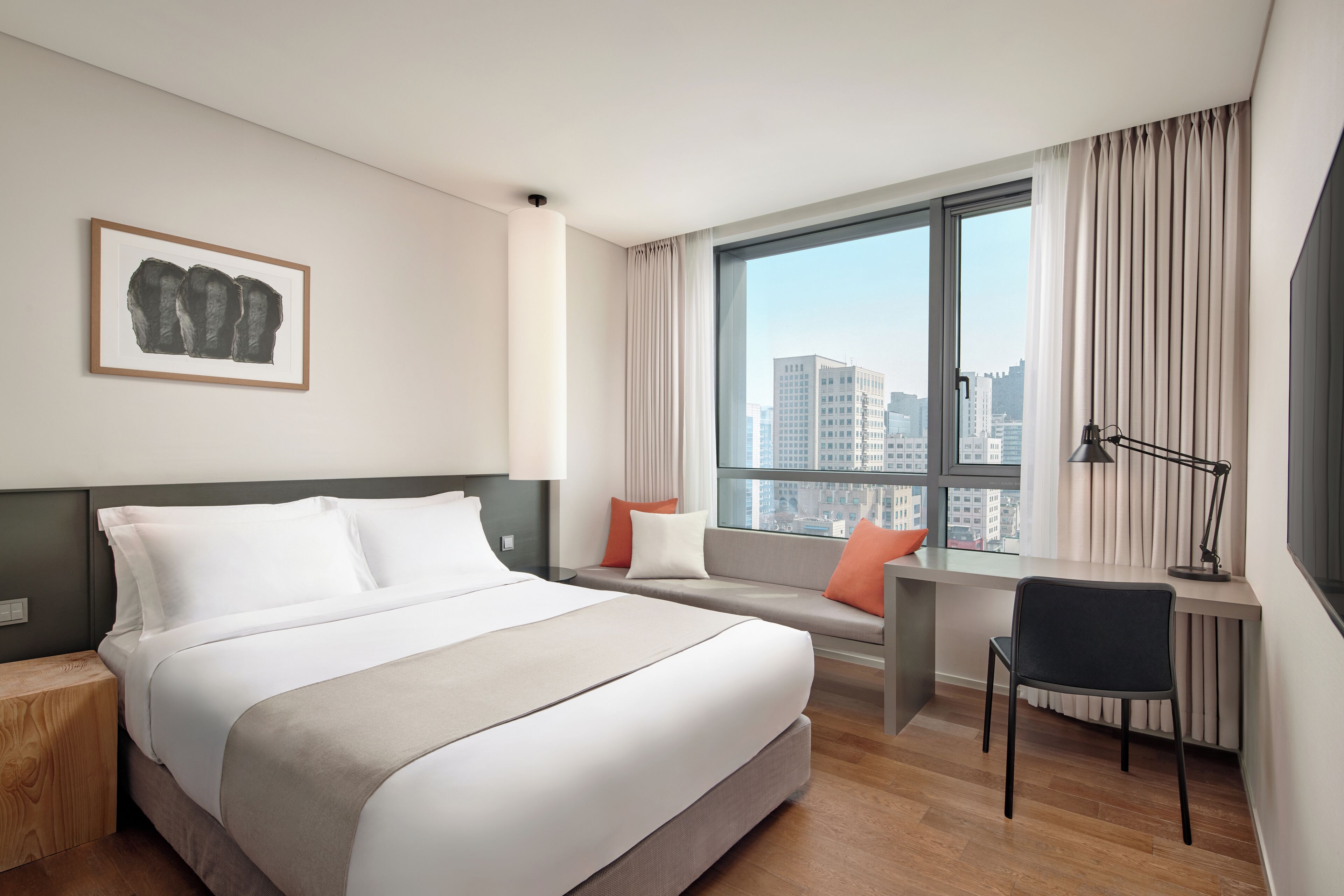 Een hotelkamer met een bed, bureau, stoel, raam met gordijnen en uitzicht op de stad.