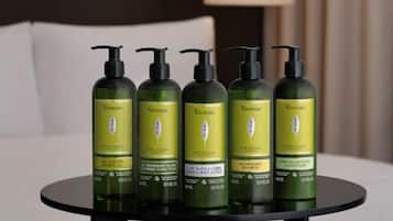 Fünf grüne Flaschen der Vervine Produkte von L'OCCITANE auf einem schwarzen Tisch.