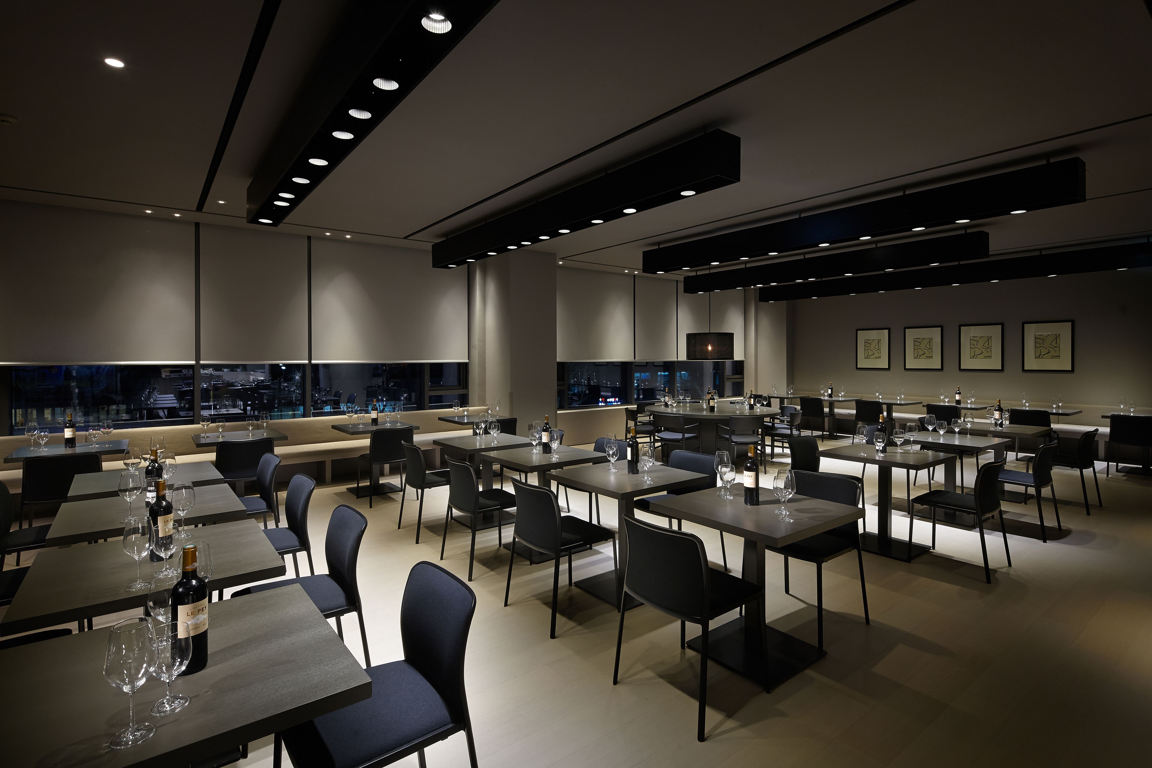 A modern restaurant with multiple tables and chairs, a bar area, and large windows offering a city view.