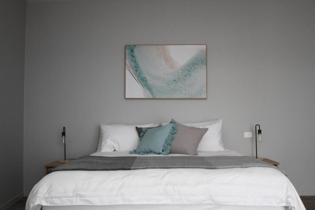 A bedroom with a bed, pillows, a blanket, and a wall-mounted abstract painting.