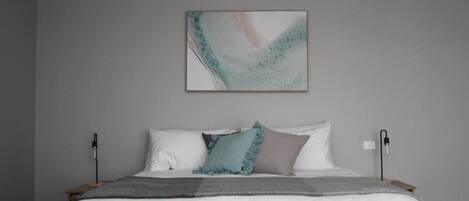 A bedroom with a bed, pillows, a blanket, and a wall-mounted abstract painting.