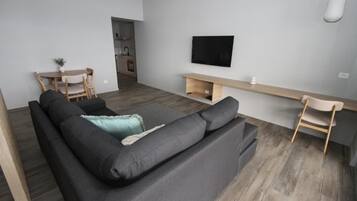 Una sala moderna con un sofá negro, un televisor montado en la pared y una mesa de comedor de madera con sillas.