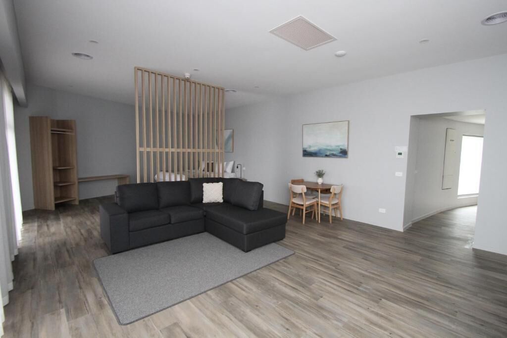 Una sala de estar moderna con un sofá modular, una mesa de comedor con sillas, piso de madera y un ventanal grande.