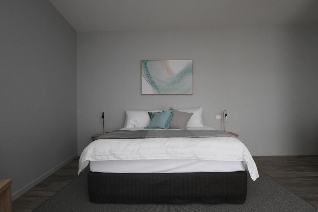 A bedroom with a bed, pillows, a blanket, a bedside table, and a wall-mounted lamp.