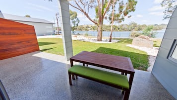 Un patio con una mesa y banca de madera, vistas a un lago y una zona verde con árboles.