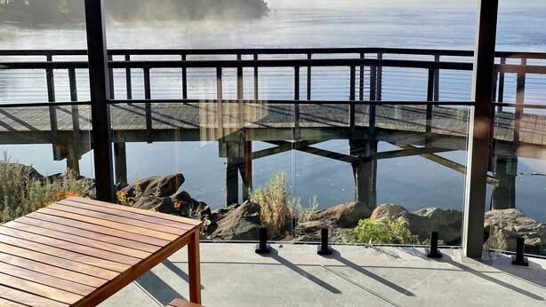 Mesa e banco de madeira em um deck de concreto, com vista para um lago nevoento e uma ponte.