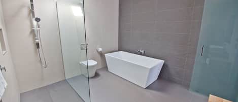 Un baño moderno con cabina de ducha de vidrio, una bañera blanca y un inodoro.