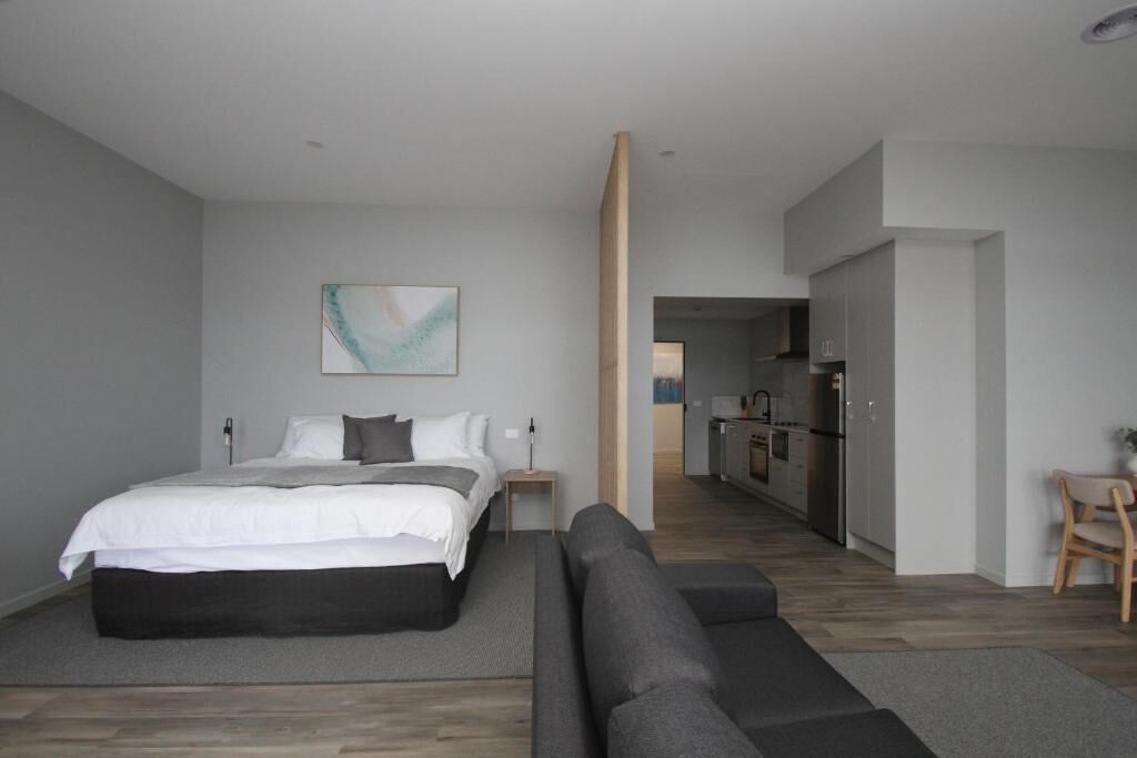 Un dormitorio moderno con una cama grande, un sofá, una mesita y un cuadro en la pared.