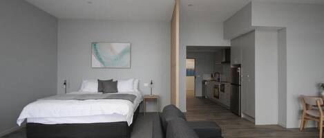 Un dormitorio moderno con una cama grande, un sofá, una mesita y un cuadro en la pared.