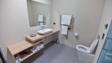 A modern bathroom with a sink, mirror, towel rack, and toilet.