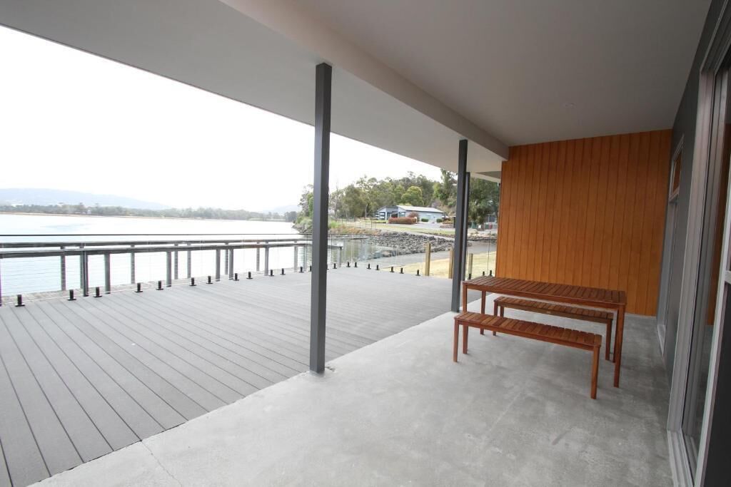 A balcony with a view of the water, a wooden bench, and a concrete floor.