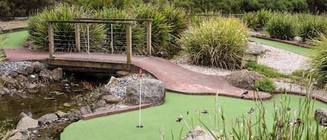 Un campo de mini golf con un puente, fuente de agua y diversas plantas.