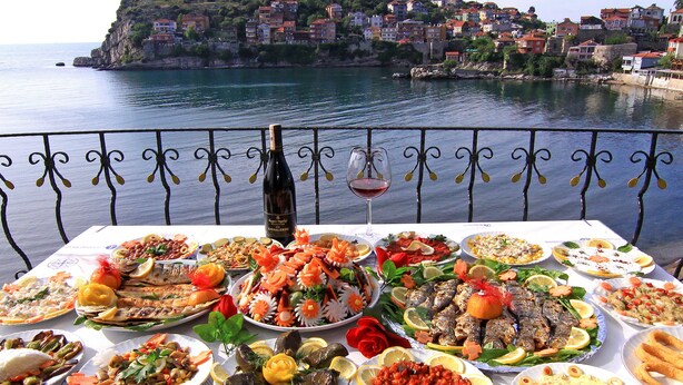 Una mesa con varios platos y una botella de vino, con vistas a un pueblo costero.