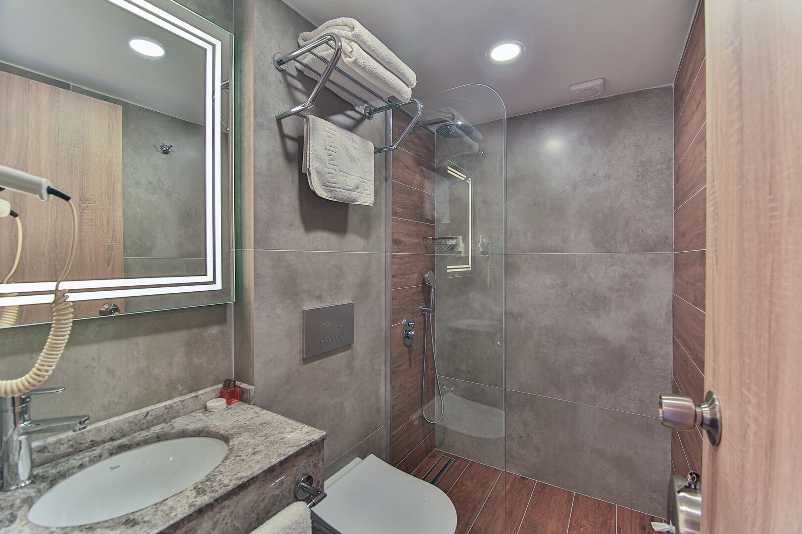 Un baño moderno con cabina de ducha de vidrio, tocador doble y espejo con luz.